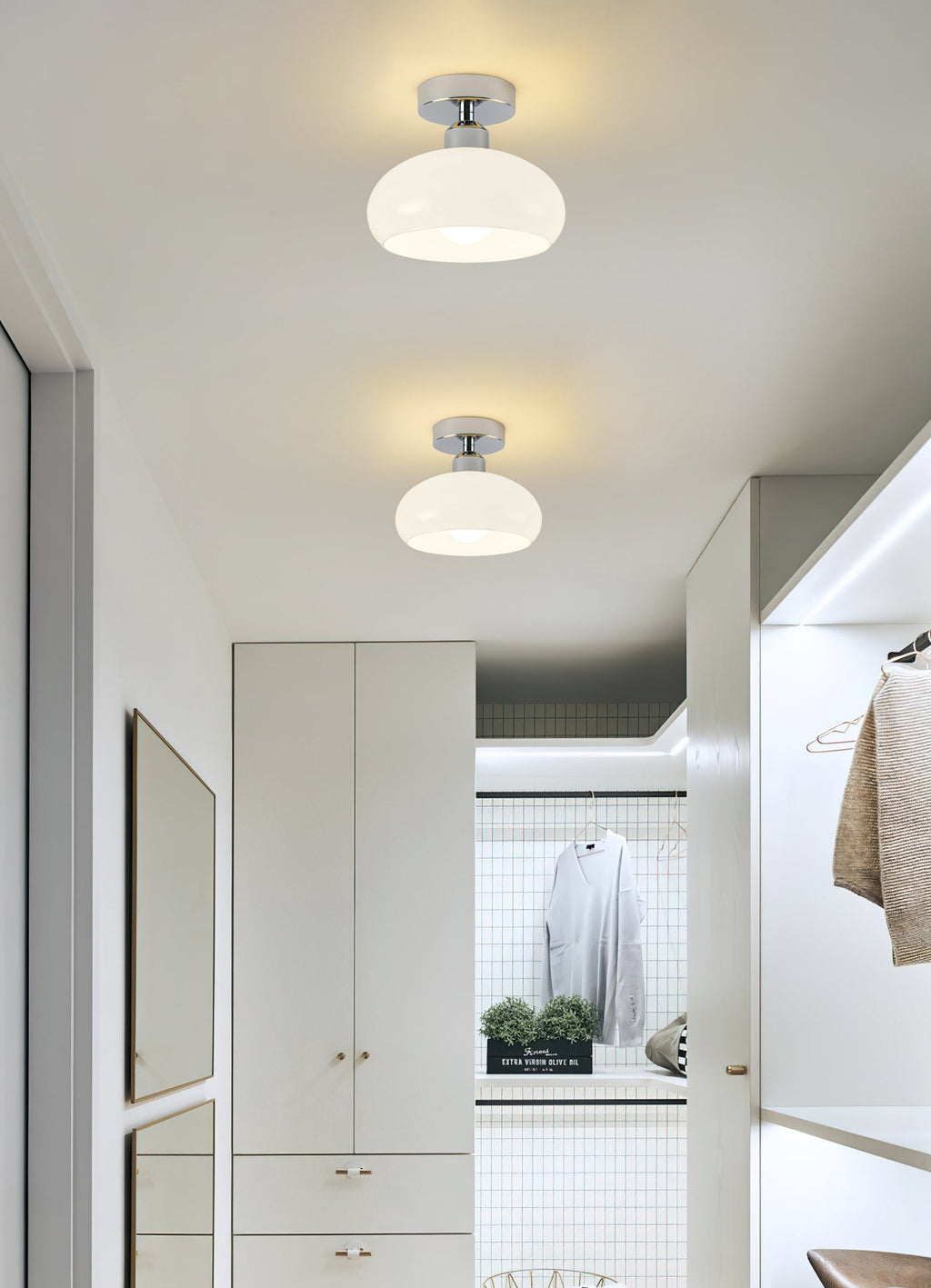 Two white glass Clérachic ceiling lights in a hallway leading to a dressing area with a hanging rail and shelves.
