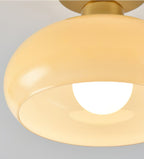 Close view of the curved beige glass shade and brass canopy on this Clérachic ceiling light, with the bulb glowing inside.
