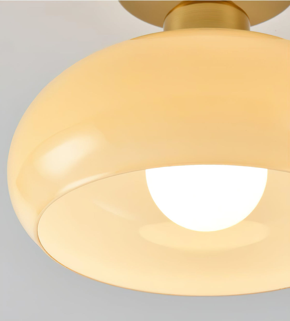Close view of the curved beige glass shade and brass canopy on this Clérachic ceiling light, with the bulb glowing inside.
