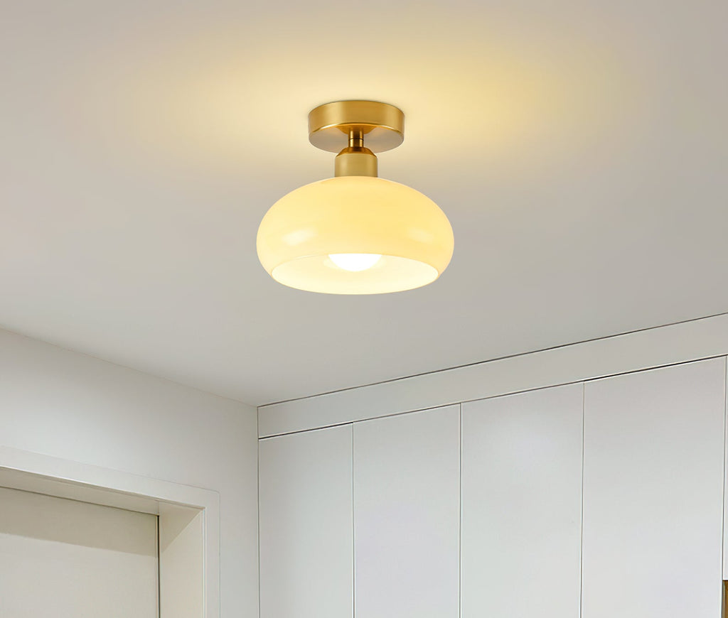 Lit beige glass Clérachic ceiling light mounted above a white wardrobe wall in a bright, minimal room.