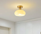 Lit beige glass Clérachic ceiling light mounted above a white wardrobe wall in a bright, minimal room.