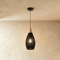 Clérachic black rattan pendant light in a teardrop cage shade with a beige wood cap over a warm plaster wall.