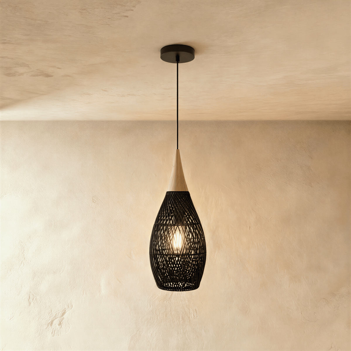 Clérachic black rattan pendant light in a teardrop cage shade with a beige wood cap over a warm plaster wall.