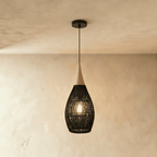 Clérachic black rattan pendant light with a woven teardrop shade and beige wood cap, viewed against a plaster wall.