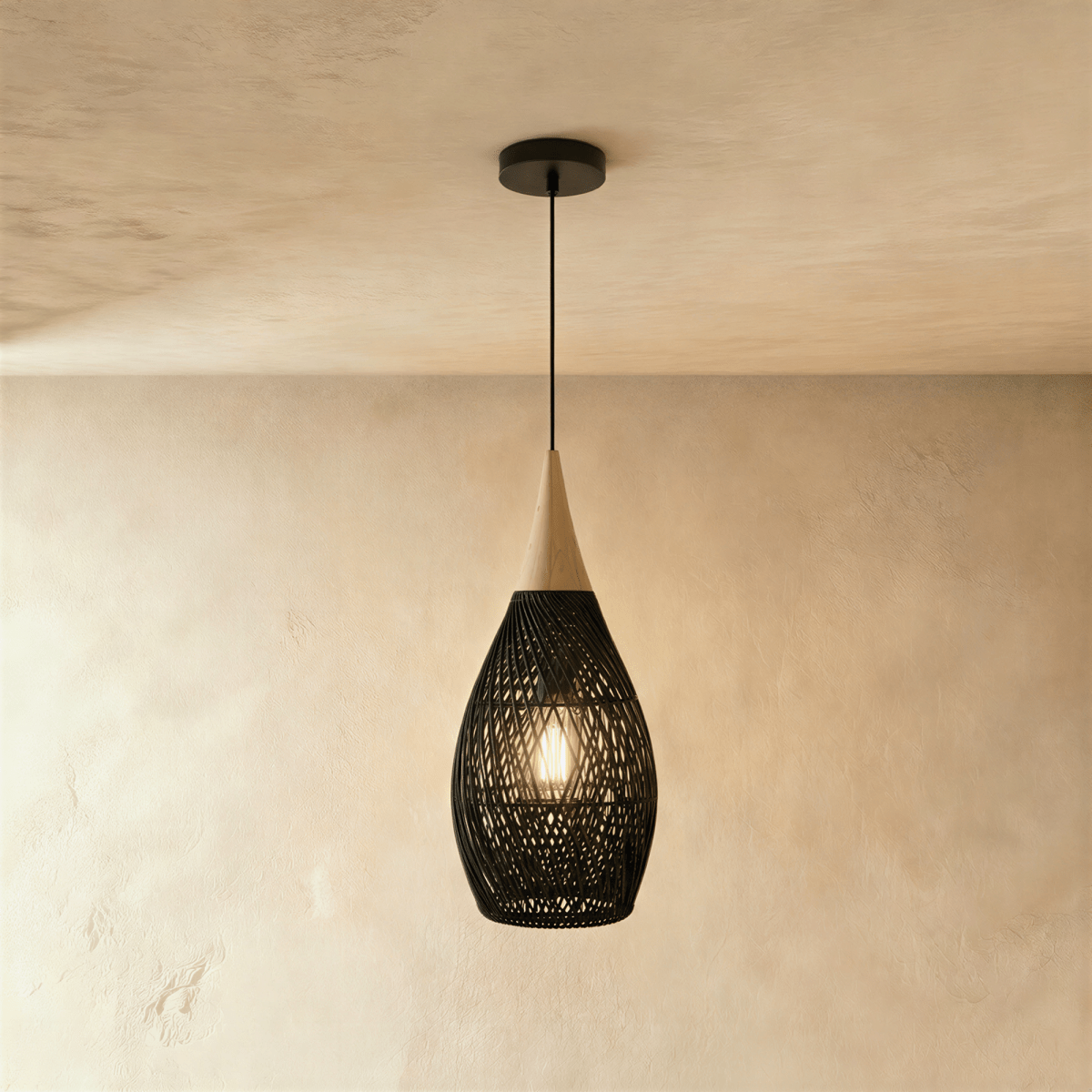 Clérachic black rattan pendant light with a woven teardrop shade and beige wood cap, viewed against a plaster wall.