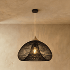 Clérachic black rattan pendant light in a wide woven dome shade with a beige wood cap against a plaster wall.