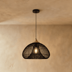 Clérachic black woven rattan dome pendant light with a beige wood cap, lit and hanging near a plaster wall.