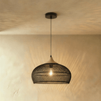 Clérachic black woven rattan pendant light with a rounded dome shade and beige wood cap, lit against plaster.