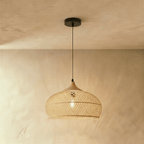 Clérachic natural rattan pendant light with a beige woven dome shade and wood cap hanging over a plaster interior.
