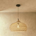 Clérachic natural rattan pendant light with a woven beige dome shade and matching wood cap, lit near a plaster wall.