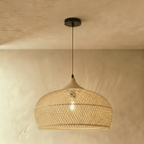 Clérachic natural rattan pendant light with a rounded beige dome shade and wood cap hanging against a plaster wall.