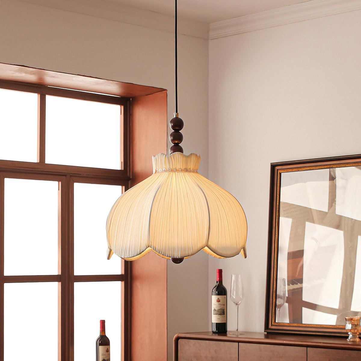 Lit Clérachic pleated pendant with walnut beads, beside a wood-framed window and a sideboard holding a bottle of red wine.