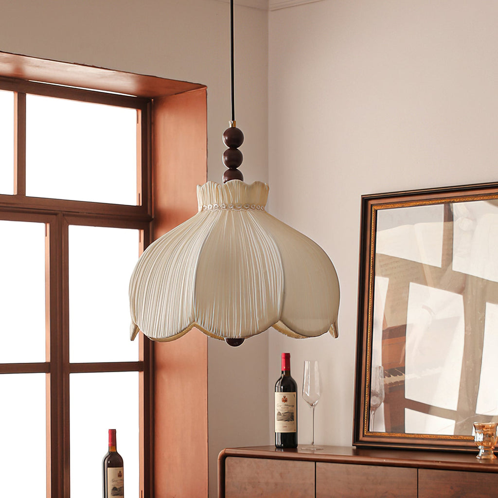 Unlit beige Clérachic pendant with a petal-shaped pleated shade, in front of a dark window frame and a gilt mirror.