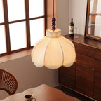Low view of a lit Clérachic pleated pendant beside a tall window, with a walnut cabinet and a dining table below.