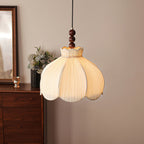 A Clérachic pleated fabric pendant in warm light above a walnut chest with a vase of flowers and a mirror.