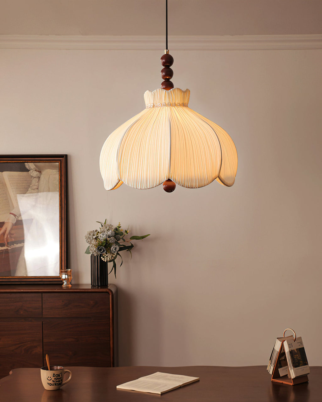 Smaller view of a lit Clérachic beige pendant in a dining corner, with a walnut sideboard and flowers behind.