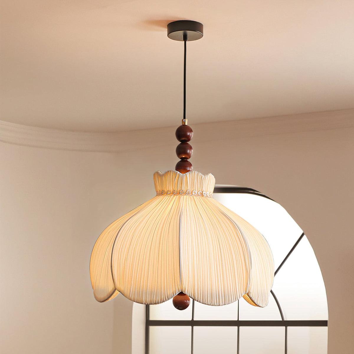 Looking up at a Clérachic pleated pendant on a black canopy, glowing in front of an arched window.