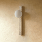 Clérachic travertine column wall light with an opal white globe switched off, mounted on a warm limewash-textured wall.