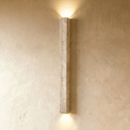 Clérachic tall travertine column wall light, no globe, with pitted natural stone and light washing up and down the wall.