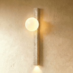 Clérachic longer travertine wall light with a lit opal globe near the top and a downlight below, on a limewash wall.