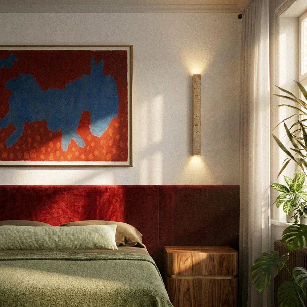 Clérachic slim travertine wall light beside a bedroom window, throwing light up and down above a red headboard and walnut nightstand.