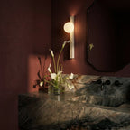 Clérachic lit globe-and-travertine wall light in a moody red bathroom with a stone vanity, black taps and calla lilies.