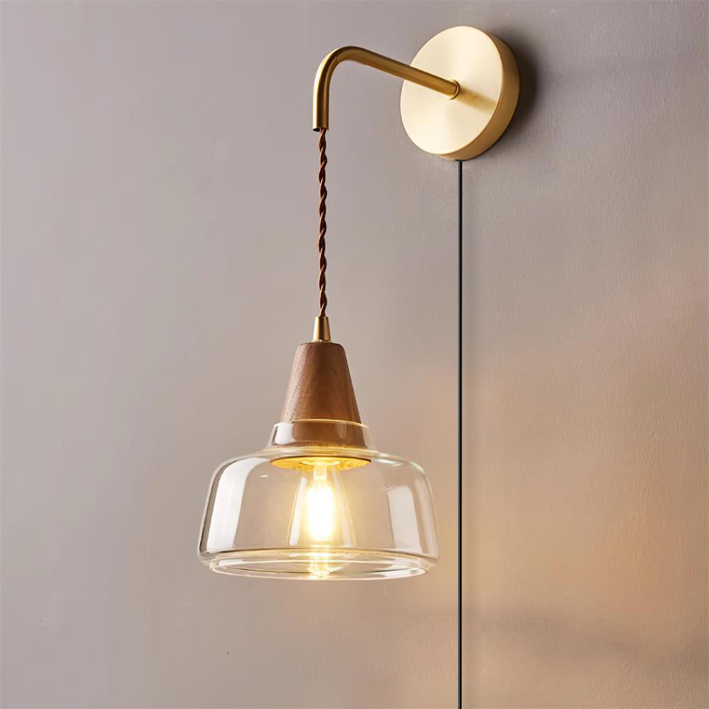 Clérachic bell glass wall sconce glowing warm against a mauve-gray wall, its brass arm and twisted cord fully visible.