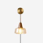 Studio shot of the Clérachic bell glass sconce lit against a white backdrop, showing the walnut cap and brass ferrule.