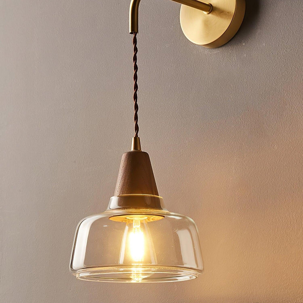 Close-up of the Clérachic sconce's clear glass bell and glowing filament bulb, seen from below against a gray wall.