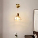 Clérachic wall sconce lit above a brown leather armchair and a small vase of white flowers in a living room corner.