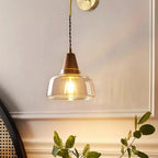 Clérachic wall sconce glowing above a wicker chair, its light warming a wainscoted wall behind green leaves.