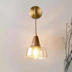 Clérachic bell sconce lit beside a glass vase of dried branches on a soft gray bedroom wall.