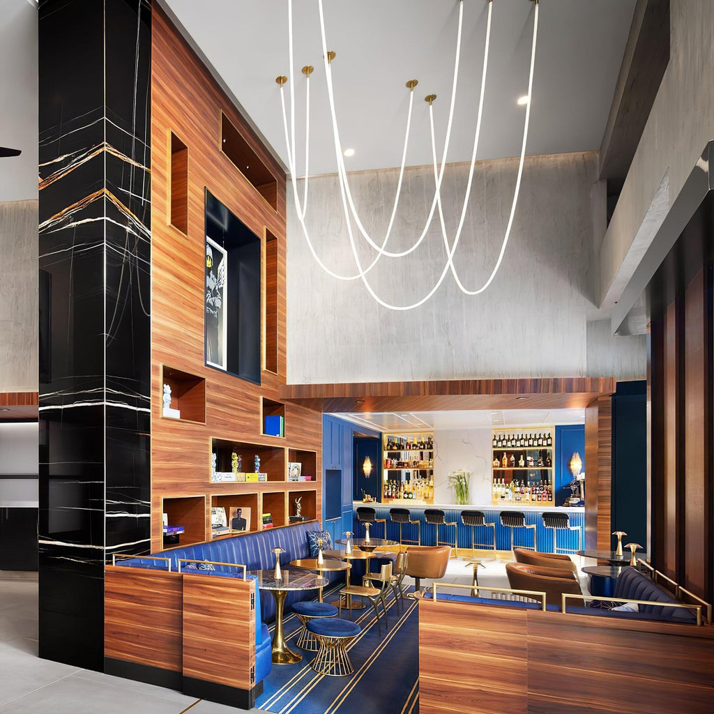 Clérachic LED rope pendants hanging in long loops from gold-toned plates above a bar with wood panelling and blue booth seating.