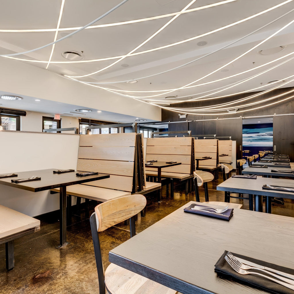Lines of light from Clérachic LED rope pendants criss-crossing a restaurant ceiling above grey tables and pale wooden booths.