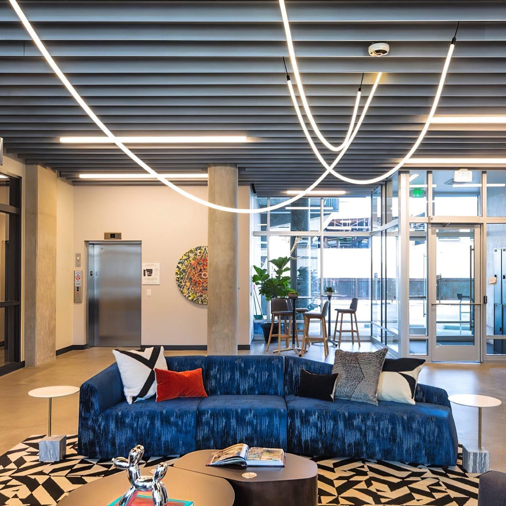 Clérachic LED rope pendants curving across a dark slatted ceiling above a blue sofa and a patterned black-and-white rug.