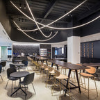 Long arcs of Clérachic LED rope light sweeping under a black ceiling above a cafe with high tables and round bar chairs.