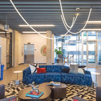 Clérachic LED rope pendants looping under a slatted grey ceiling, seen from the other side of a blue sofa and a low round table.
