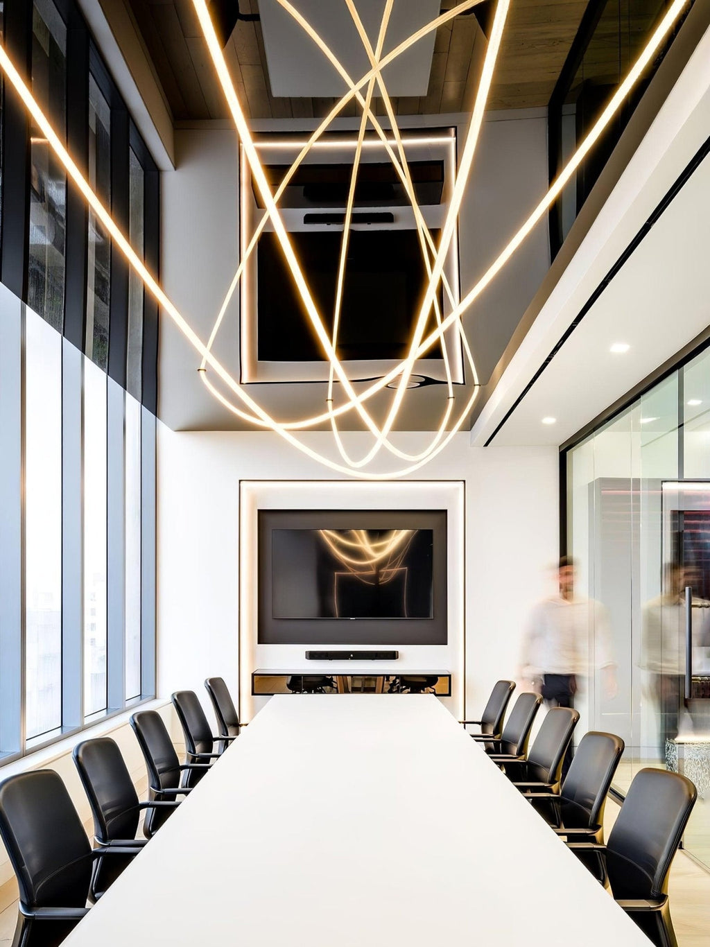 Intersecting loops of glowing Clérachic rope light above a long white table and black chairs in a meeting room with tall windows.