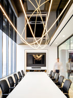 Intersecting loops of glowing Clérachic rope light above a long white table and black chairs in a meeting room with tall windows.
