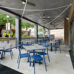 Pale Clérachic rope pendants strung across the ceiling of a covered terrace above blue chairs and square tables.