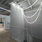Clérachic LED rope pendants forming deep, glowing loops against a grey wall and white railing in a stairwell.