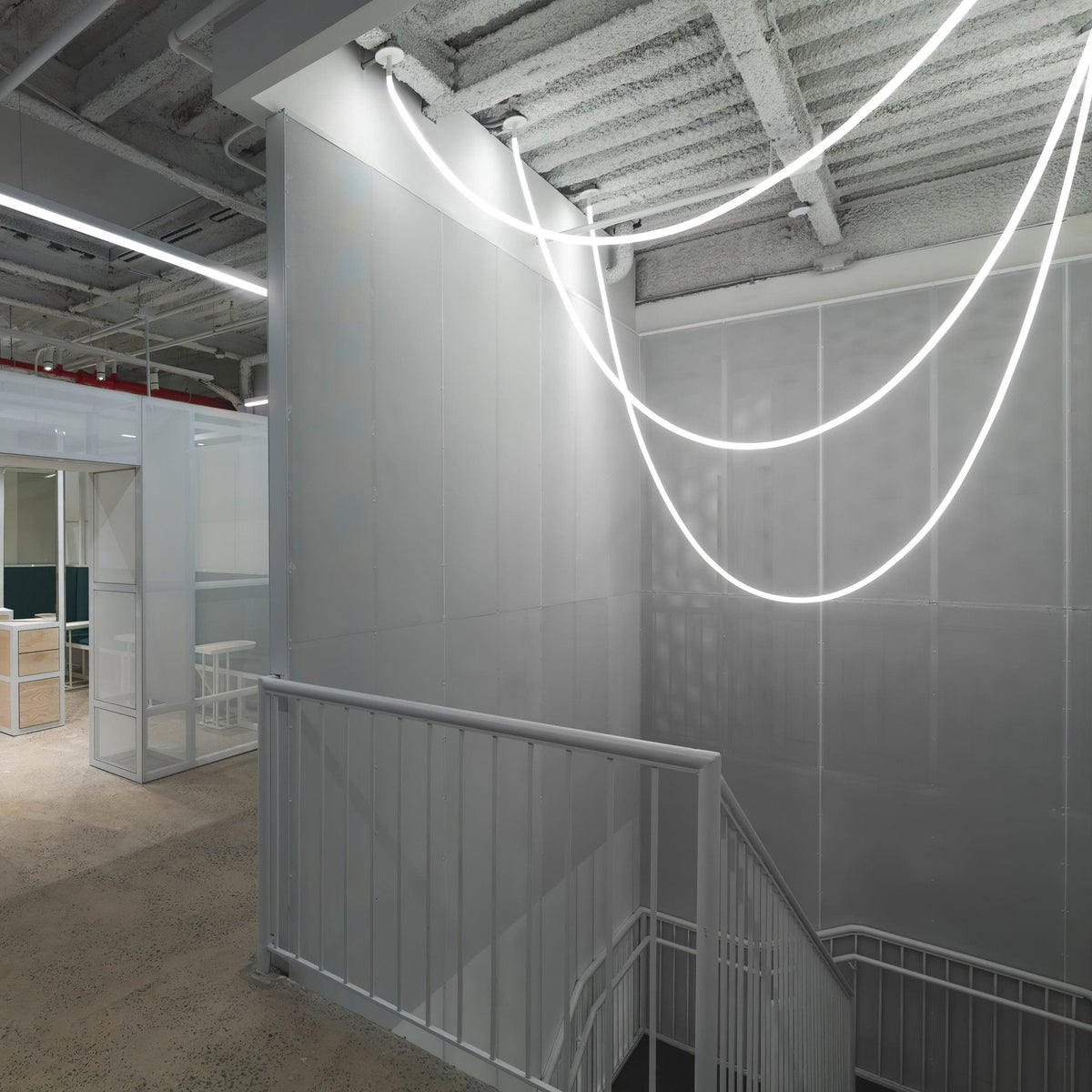 Clérachic LED rope pendants forming deep, glowing loops against a grey wall and white railing in a stairwell.
