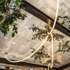 A bright Clérachic rope pendant arcing across a ceiling beam, with tree branches and a mirrored panel ceiling above.