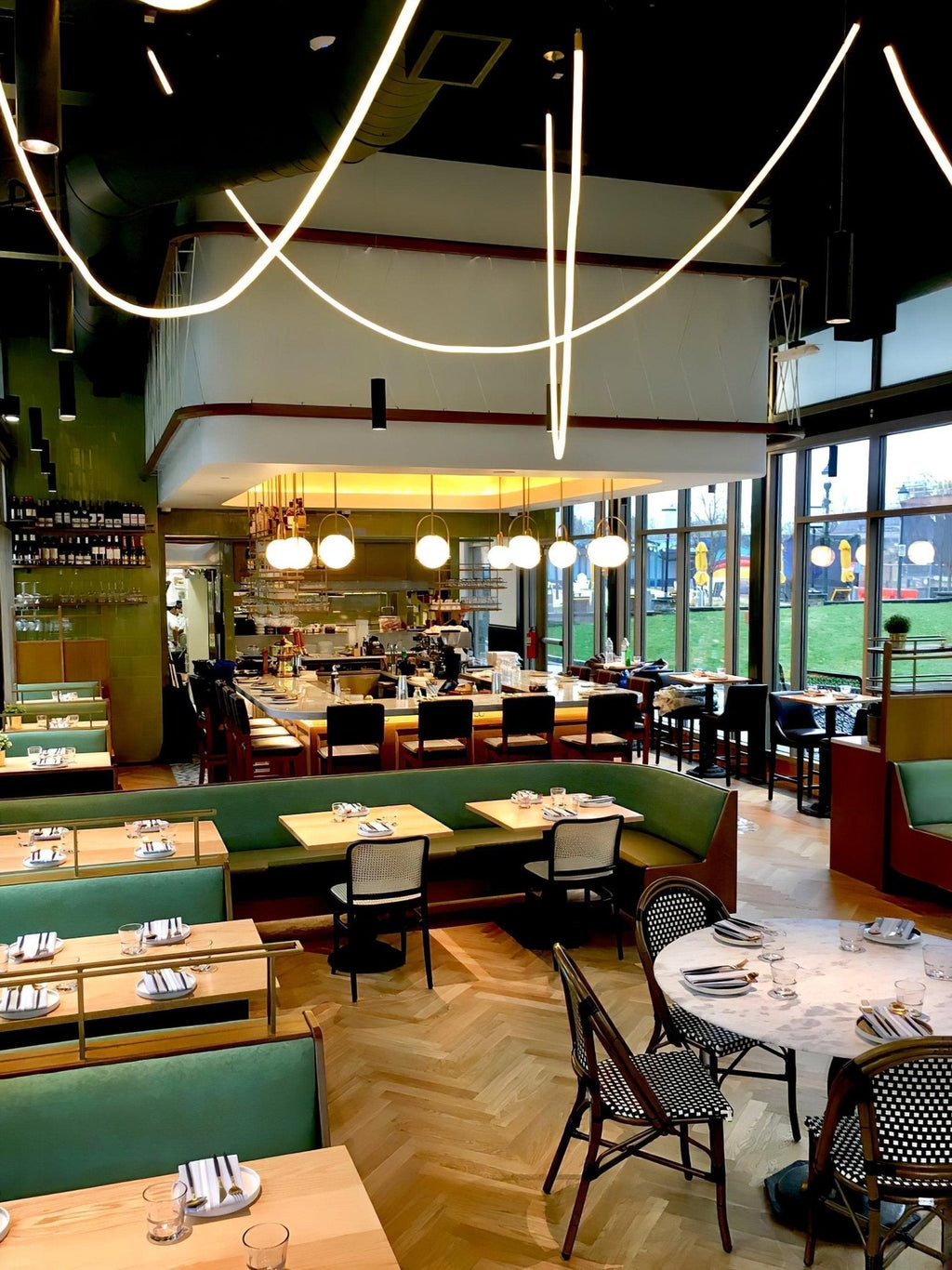Long loops of Clérachic LED rope light above a restaurant with green banquettes, a bar and herringbone flooring.