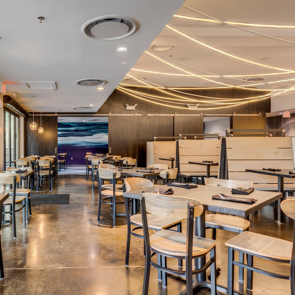 Overlapping lines of Clérachic LED rope light above a restaurant of wooden booths, bentwood chairs and a blue wall painting.