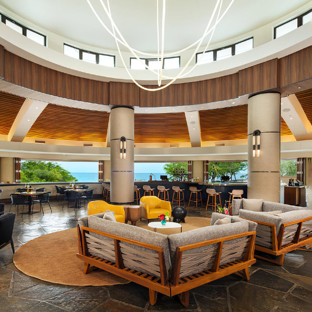 Clérachic LED rope pendants hanging from a round dome above a round lounge with wood-framed sofas and yellow chairs.