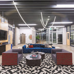A Clérachic LED rope pendant arcing across a dark industrial ceiling above a blue sofa and two grey armchairs on a patterned rug.