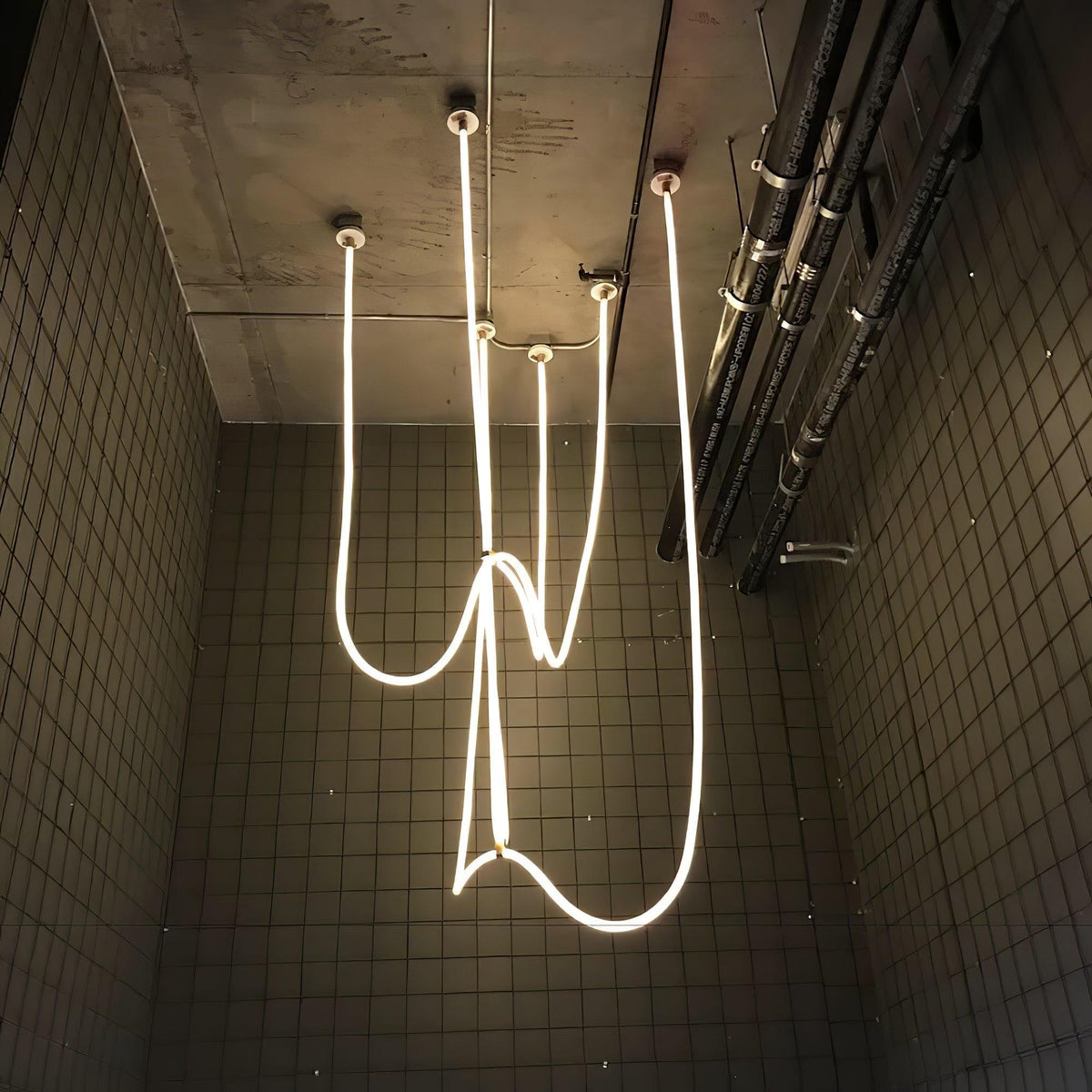 Clérachic LED rope pendants hanging in tangled, looping lines against a dark tiled wall, seen from below.