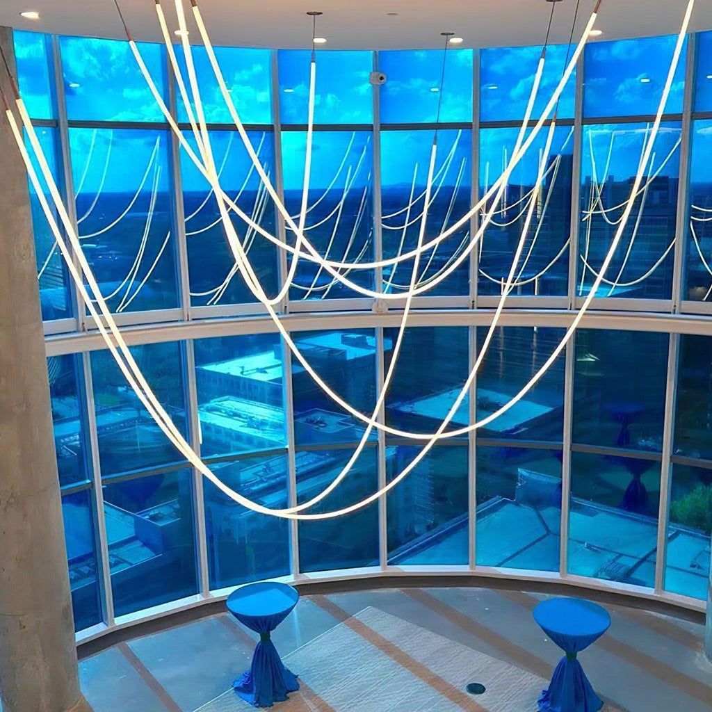 Many Clérachic LED rope pendants forming deep curves in front of a curved glass wall with a blue evening sky.