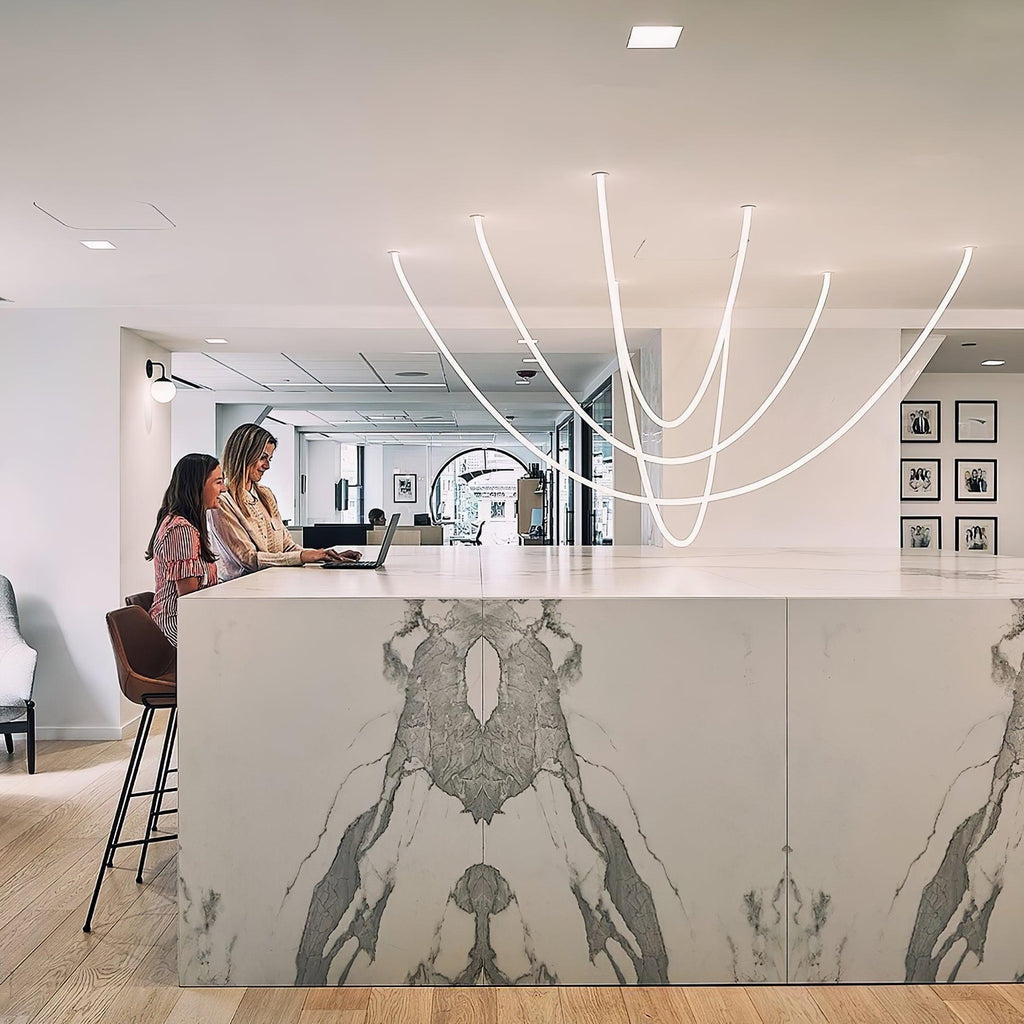 Clérachic LED rope pendants forming deep curves above a long marble-fronted counter where two people work at laptops.